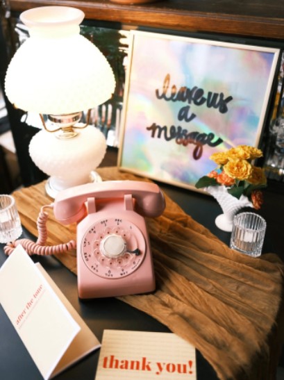 The image shows a rotary dial pink telephone, and next to it are cards showing the answering machine messages on different cards. “Leave us a message” , “After the tone” and “Thank you”
