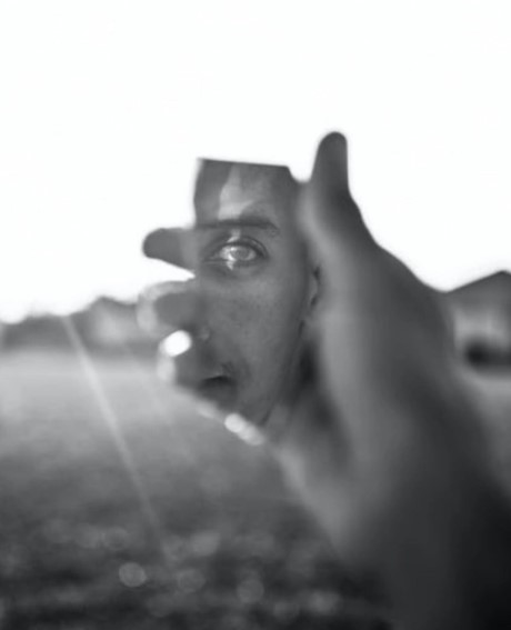 The image shows a person holding a piece of broken mirror in which their face is partially reflected.